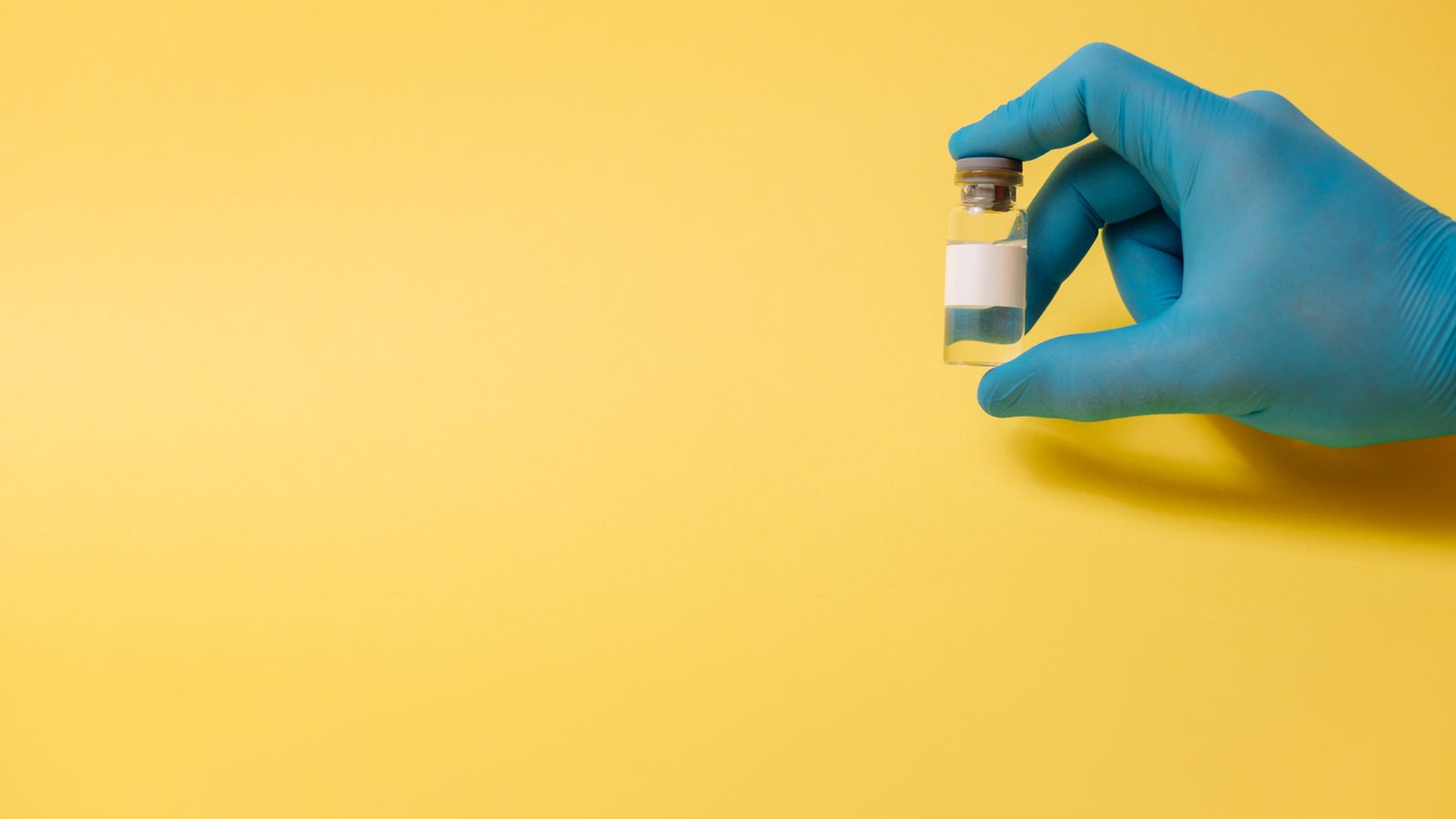 A gloved hand holds a medical vial against a bright yellow background, symbolizing health and medicine